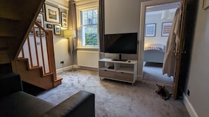 Uma sala de estar com escada, uma televisão em um móvel, um radiador e uma janela com cortinas.