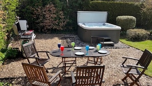 An outdoor patio with a hot tub, wooden chairs, and a table set for four with colorful drinks. - Gorgeous Comrie Cottage, hot tub & Mountain Views (Crieff)