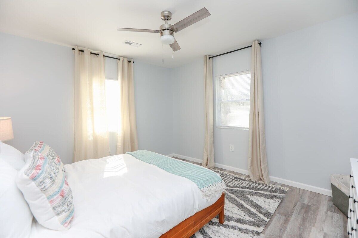 A bedroom with a bed, a ceiling fan, and a window with curtains.