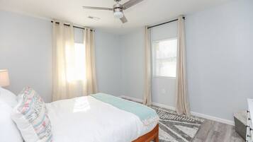 A bedroom with a bed, a ceiling fan, and a window with curtains.