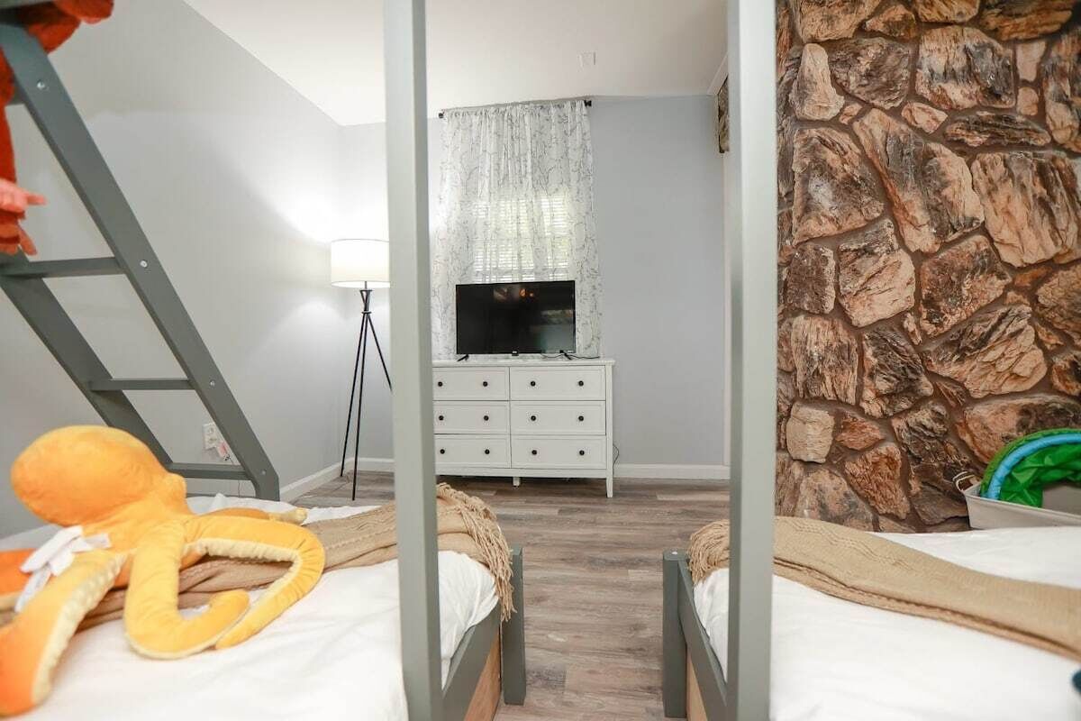 Une chambre avec deux lits, une télévision, une commode et un mur en pierre.