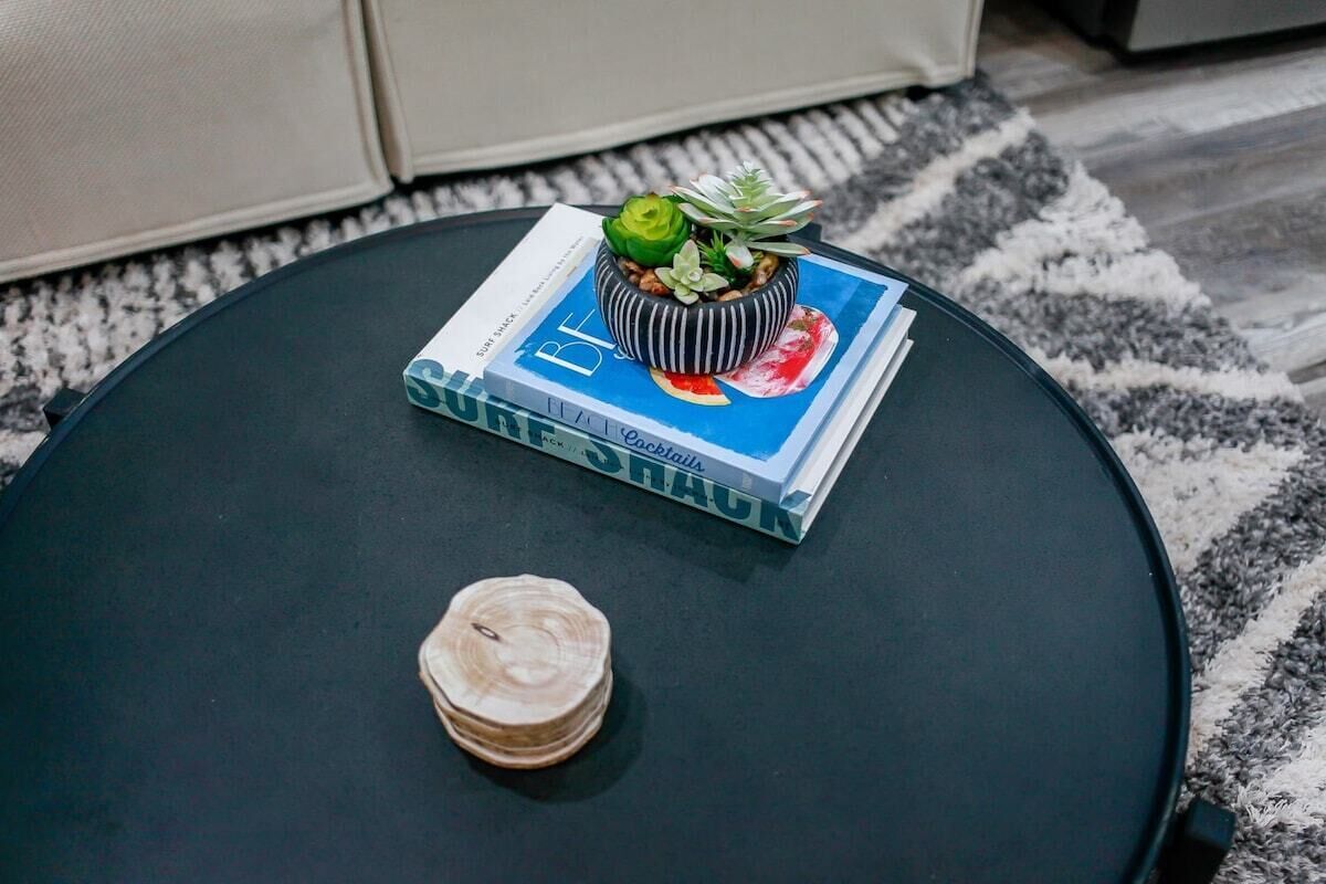 Ett runt, svart bord med en bok som heter ”Cocktails” och en liten krukväxt ovanpå.