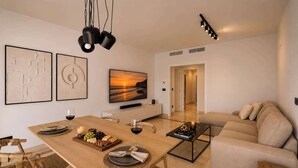 A modern living room with a wooden dining table, a sofa, and a TV on the wall.