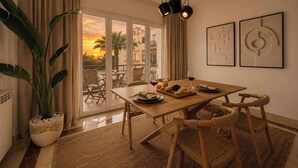 A dining area with a wooden table, wicker chairs, a potted plant, and artwork on the wall.