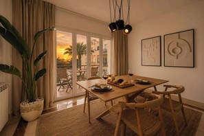 A dining area with a wooden table, wicker chairs, a potted plant, and artwork on the wall.