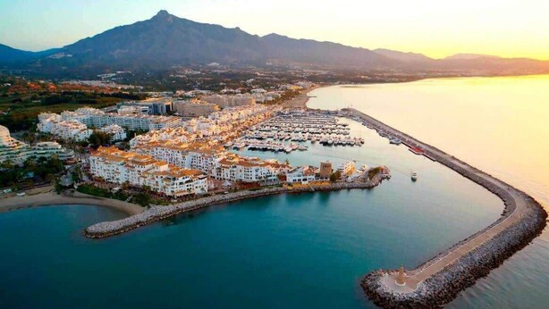 A coastal town with a marina, buildings, and a mountain in the background.