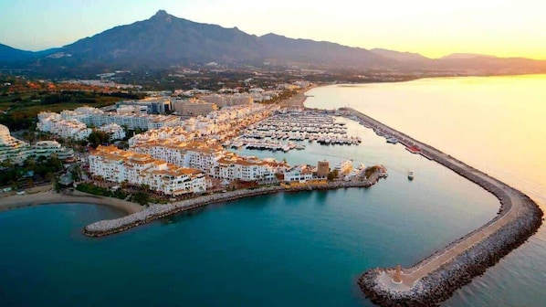 A coastal town with a marina, buildings, and a mountain in the background.