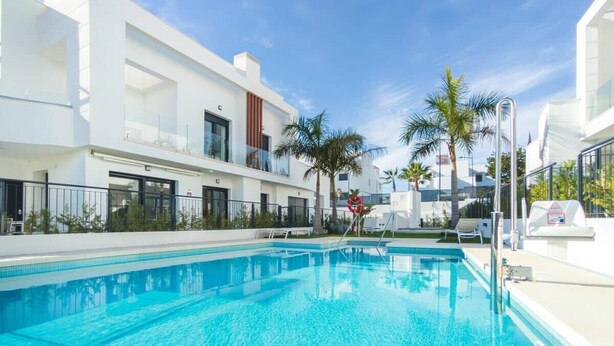 A modern hotel with a swimming pool, white exterior, and palm trees.