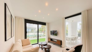 A modern living room with a sofa, two armchairs, a coffee table, and a TV on a stand.