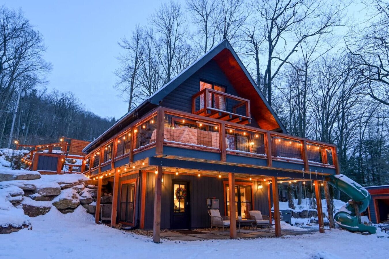 A two-story log cabin with a balcony, surrounded by snow and trees.