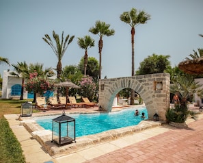 Una piscina con un arco de piedra, rodeada de palmeras y sillas de descanso.