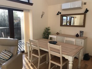 Ein Essbereich mit einem Holztisch, weißen Stühlen, einer kleinen Topfpflanze und einem Spiegel über dem Tisch.