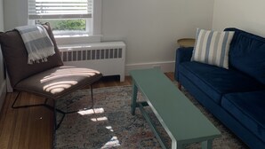 Ein Wohnzimmer mit einem braunen Sessel, einem blauen Sofa, einem hellgrünen Tisch und einem gemusterten Teppich.
