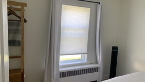 Ein Schlafzimmer mit einem Fenster, das mit weißen Vorhängen verziert ist, einem Heizkörper und einem Holzschrank.