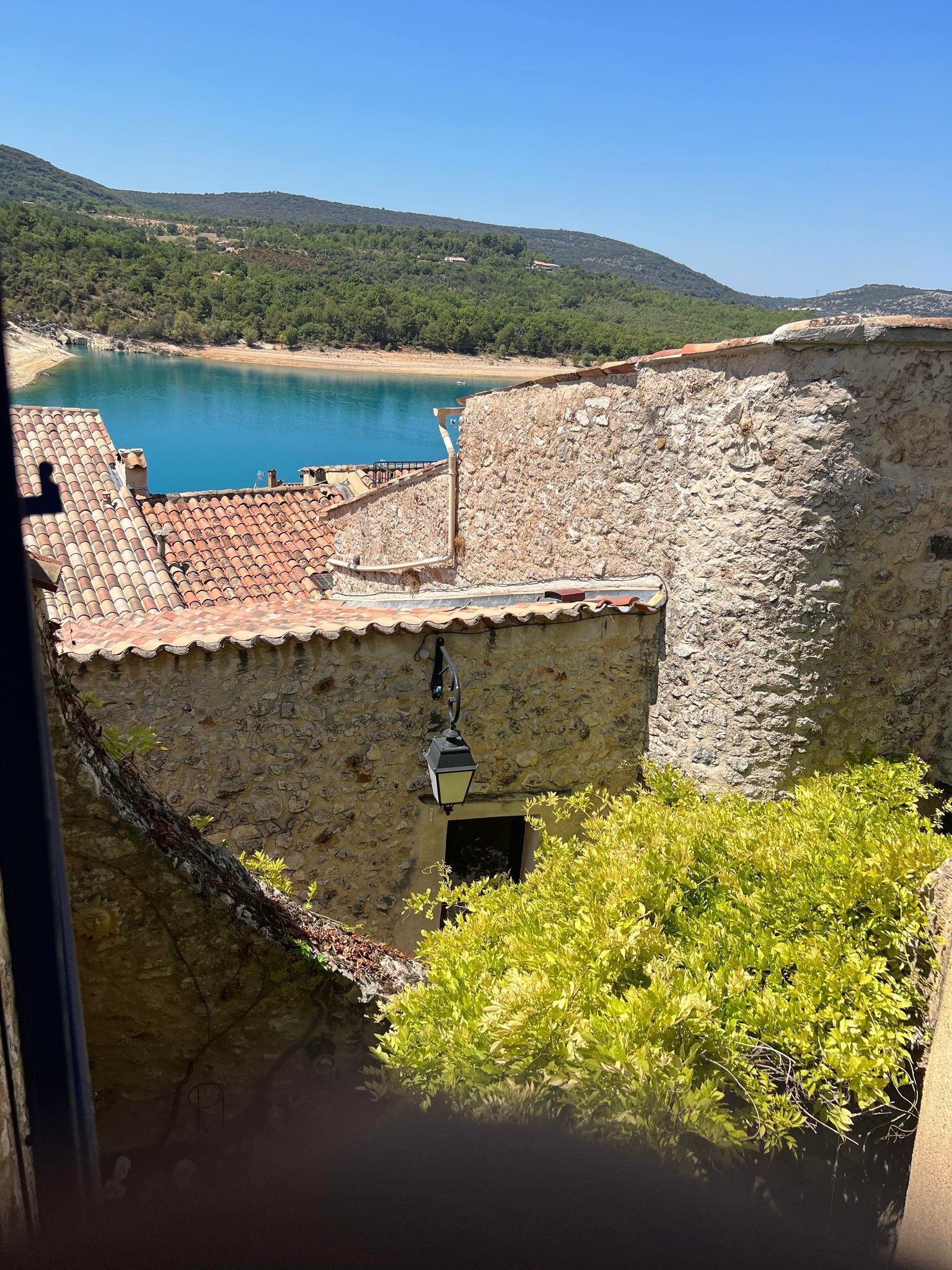 A stone building with a tiled roof overlooking a body of water and a hilly landscape.