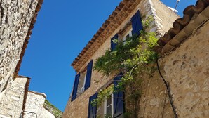 A narrow street with stone buildings, one with a visible window and blue shutters, and a street lamp.