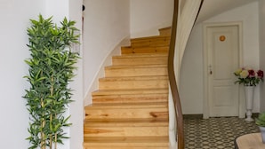 A staircase with wooden steps leading to a landing, a potted plant, and a patterned floor. - Lalitana Townhouse (Lagos)