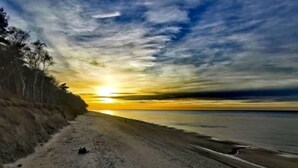Una playa con un sendero que lleva al agua, árboles a la izquierda y una puesta de sol al fondo.