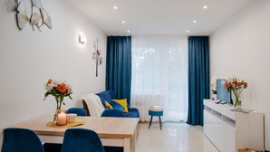 Una sala de estar moderna con comedor, que incluye un sofá, una mesa de centro y un televisor sobre un mueble blanco.