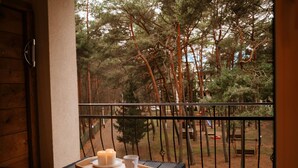 Un balcón con vista a una zona boscosa, una mesa con velas y una puerta de madera.
