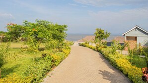 A paved pathway flanked by lush greenery and a building with a brick facade. - GALORE LUXURY RESORT (Kisumu)