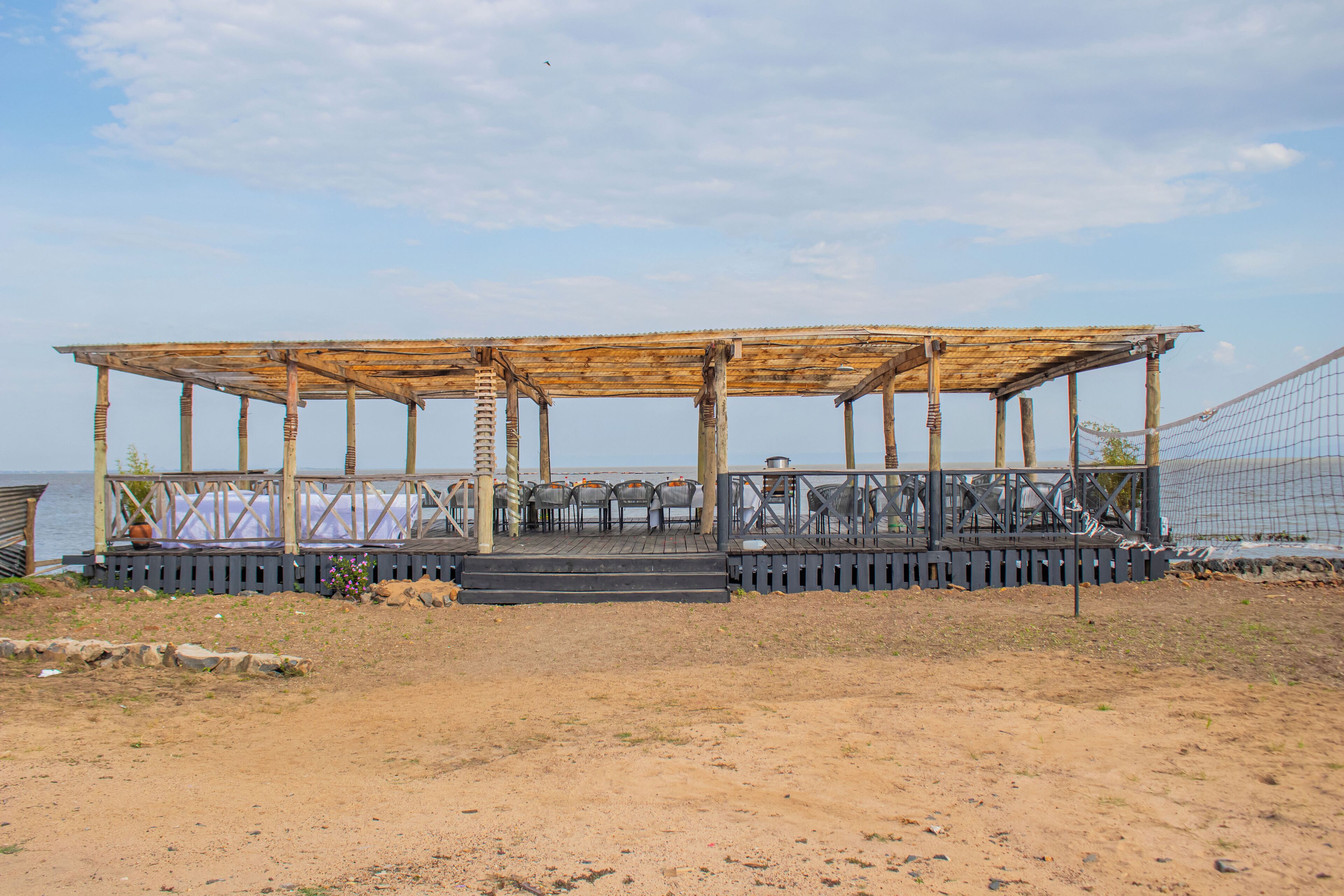 Un espace extérieur aménagé avec des sièges en bois, offrant une vue sur la mer, et comprenant une scène simple ainsi que des chaises.