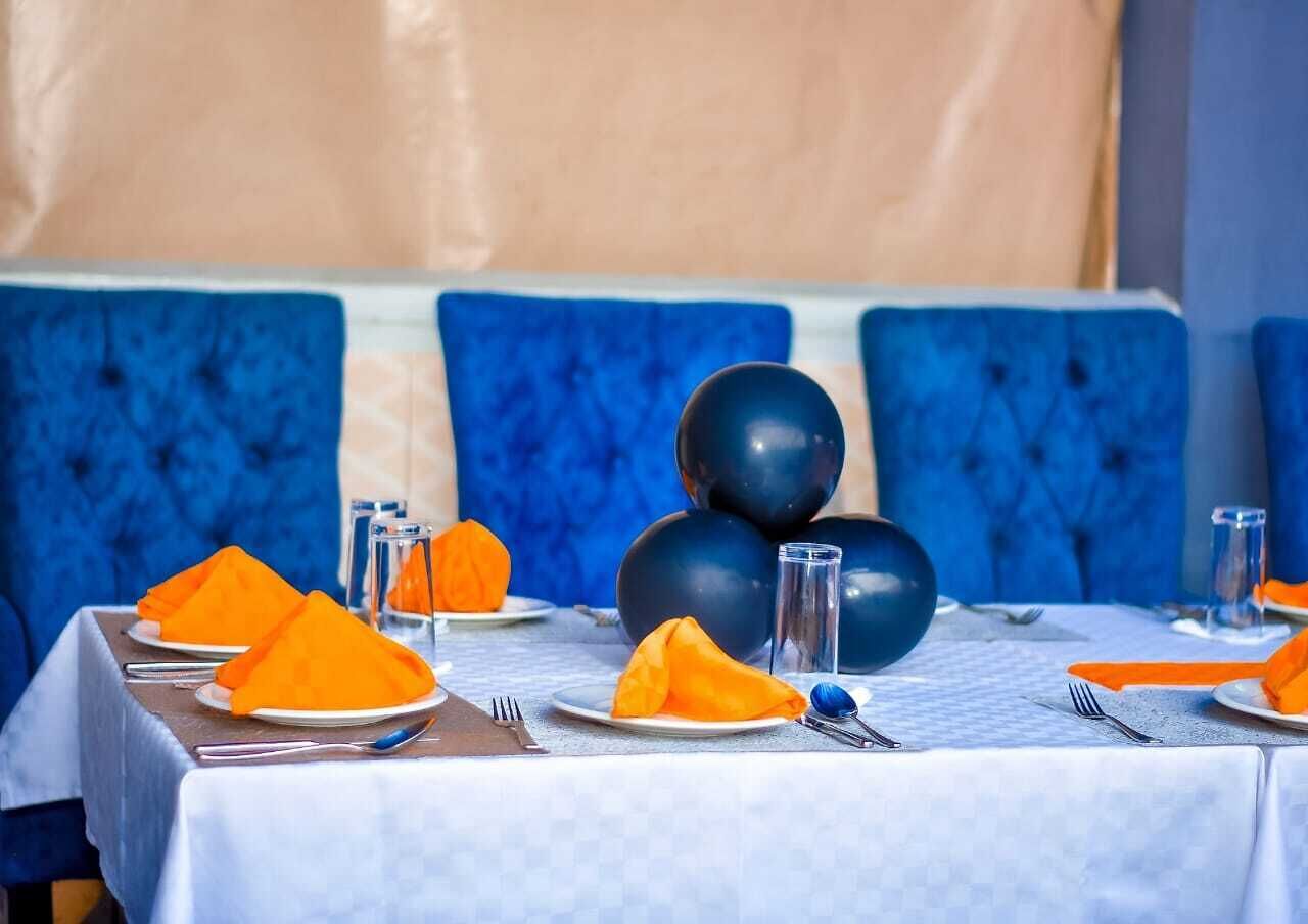 Mesa de comedor dispuesta con sillas tapizadas en azul, platos y servilletas anaranjadas.