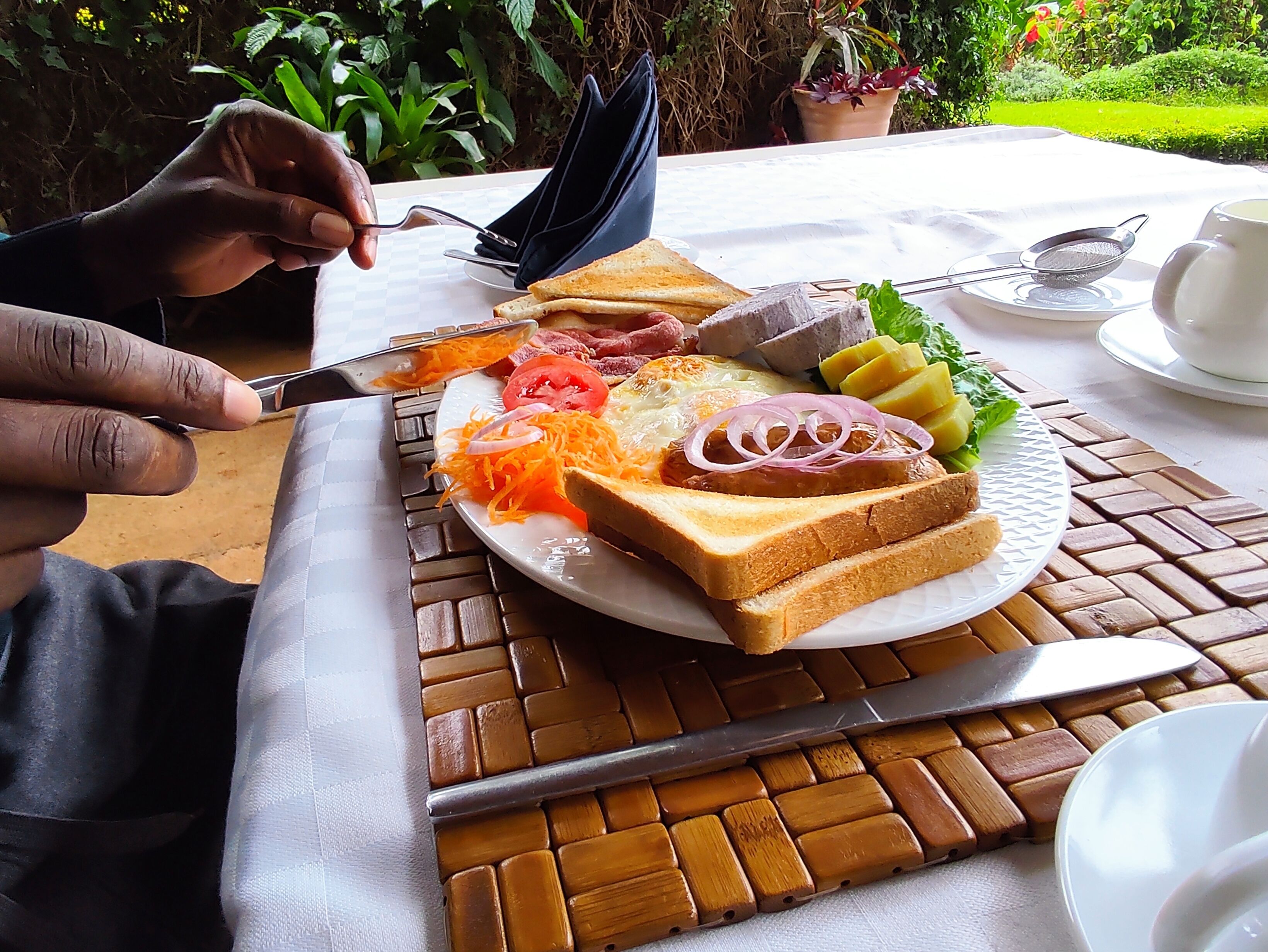 Un desayuno con tostadas, huevos y vegetales sobre una mesa al aire libre.