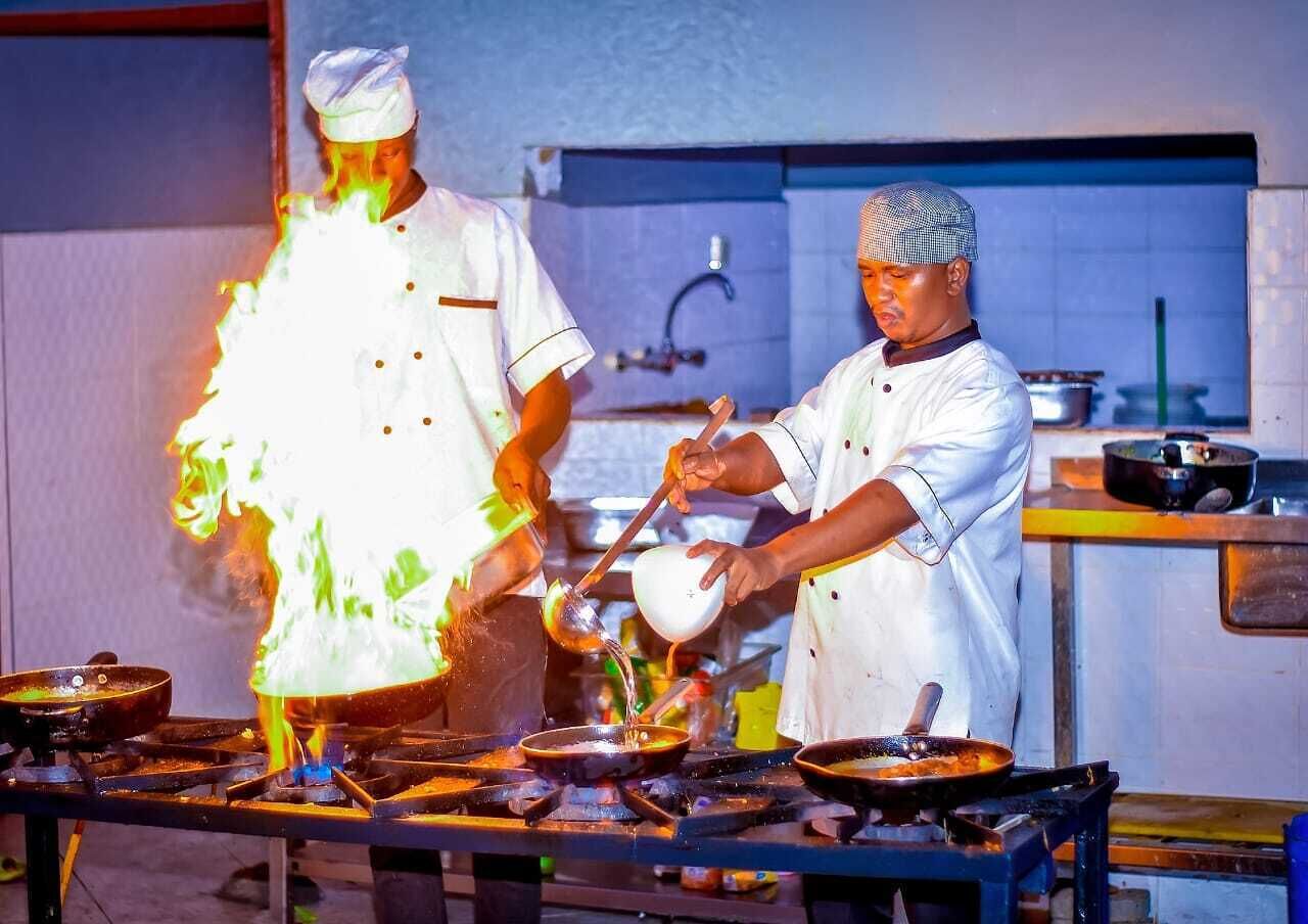Des chefs dans une cuisine équipée de plusieurs postes de cuisson, avec un robinet visible à l’arrière-plan.