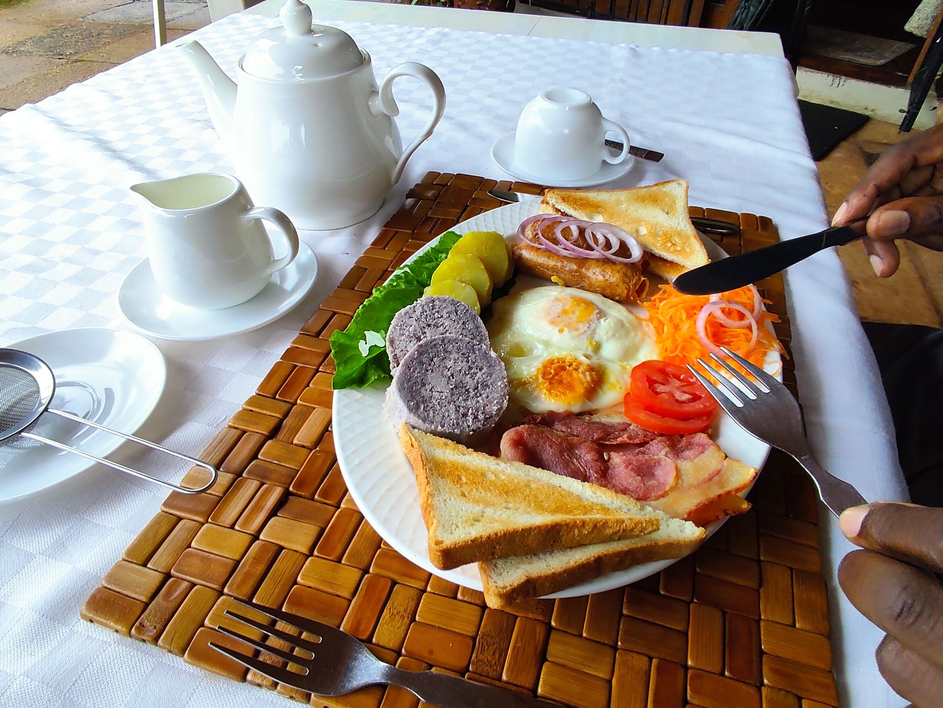 A breakfast plate with toast, eggs, ham, and vegetables on a woven placemat.