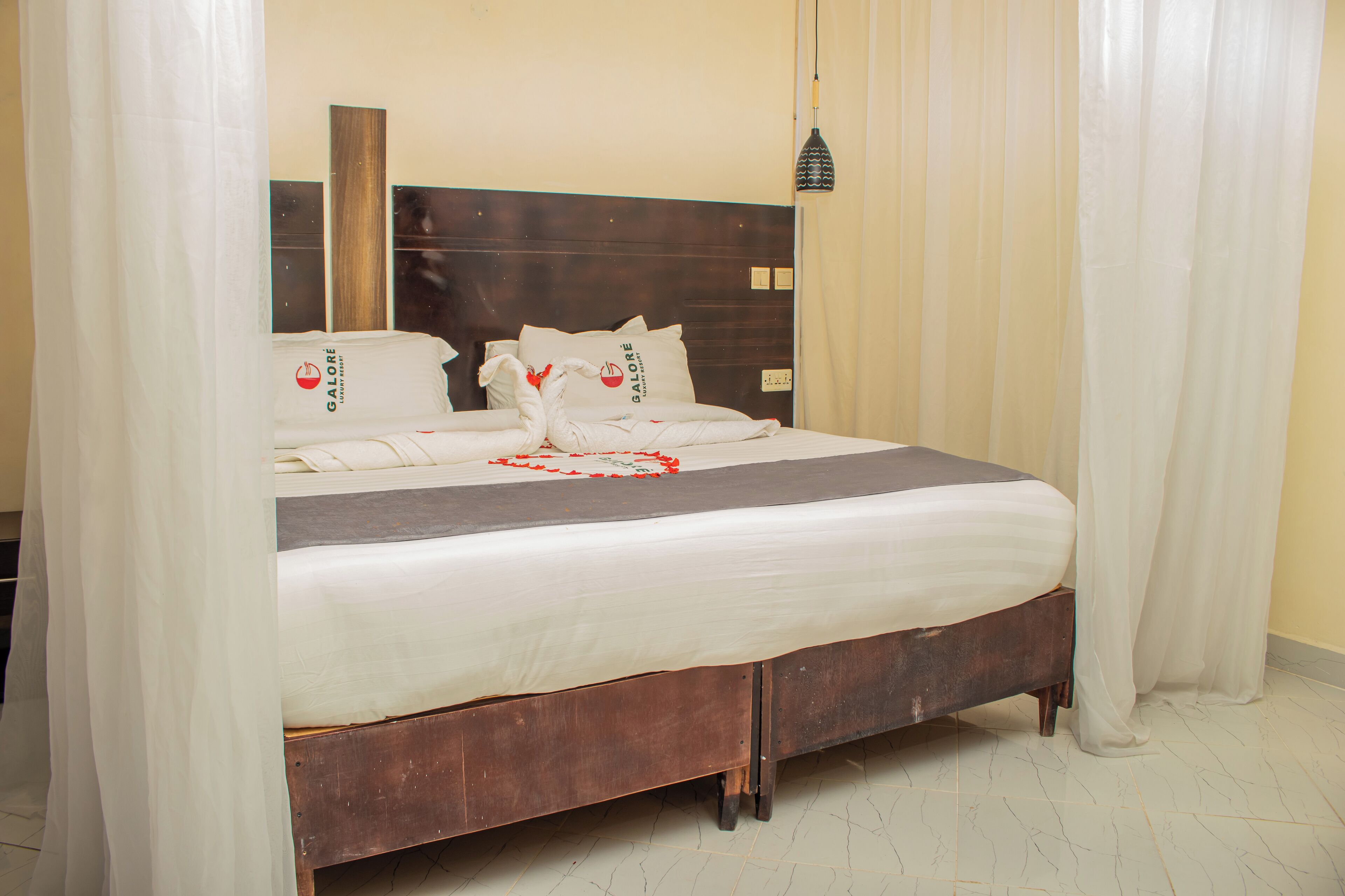 A neatly made bed with white linens and decorative pillows, a wooden headboard, and sheer curtains.