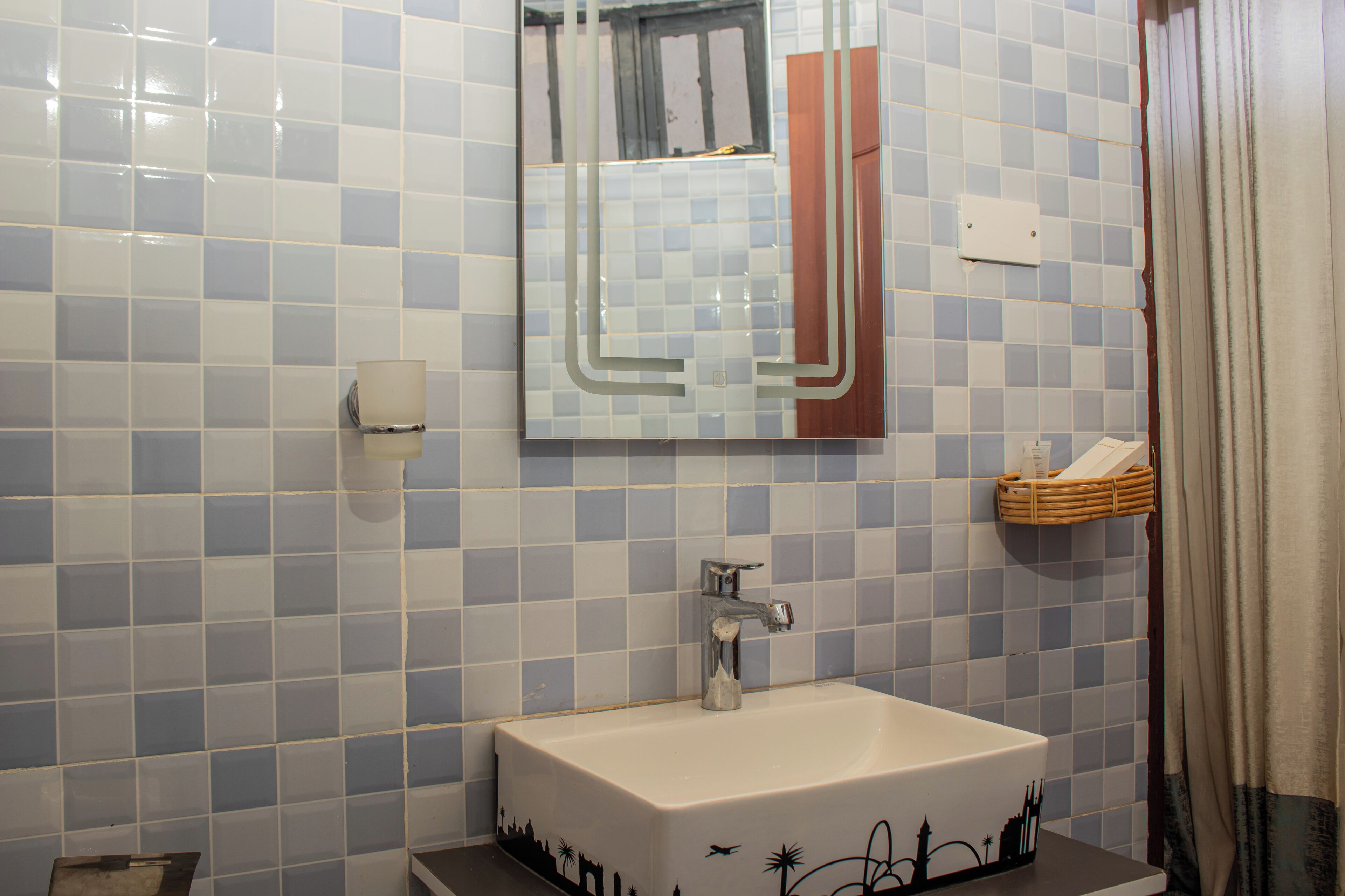 A bathroom with a tiled wall, a sink, a mirror, and a towel rack.