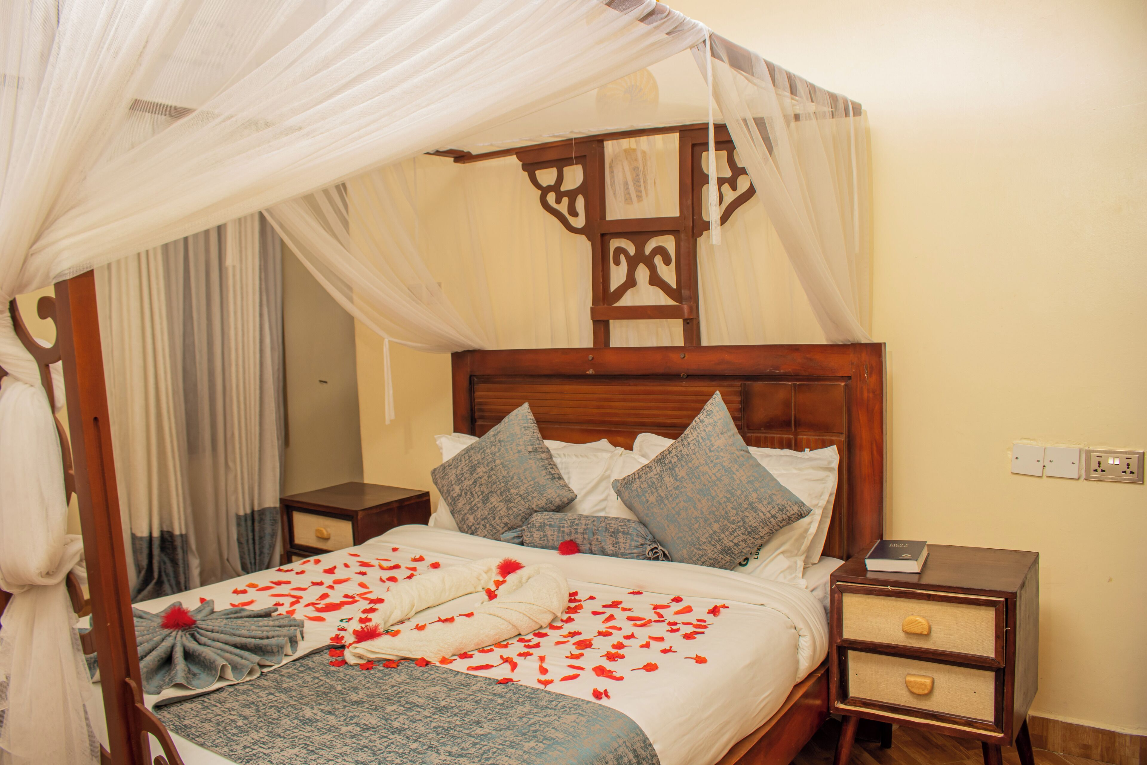 A neatly made bed with a canopy, pillows, and a bedside table with a book.