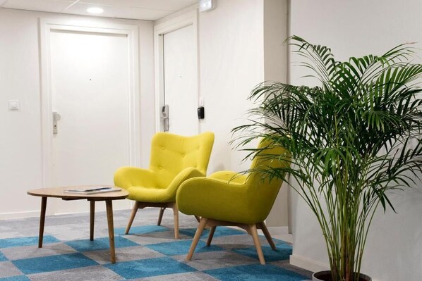 Una habitación con dos sillones amarillos, una mesita de madera y una planta grande en maceta.