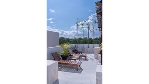 Relax on the rooftop terrace with comfortable lounge chairs and a small table, surrounded by lush greenery and a modern design.