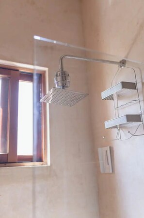 Une douche avec un pommeau amovible, une fenêtre et une étagère fixée au mur.
