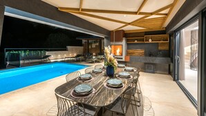 Un área de comedor moderna al aire libre con piscina, chimenea y vistas al exterior.