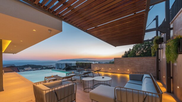 Un área de lounge moderna al aire libre con piscina, asientos y vistas al atardecer sobre el océano.