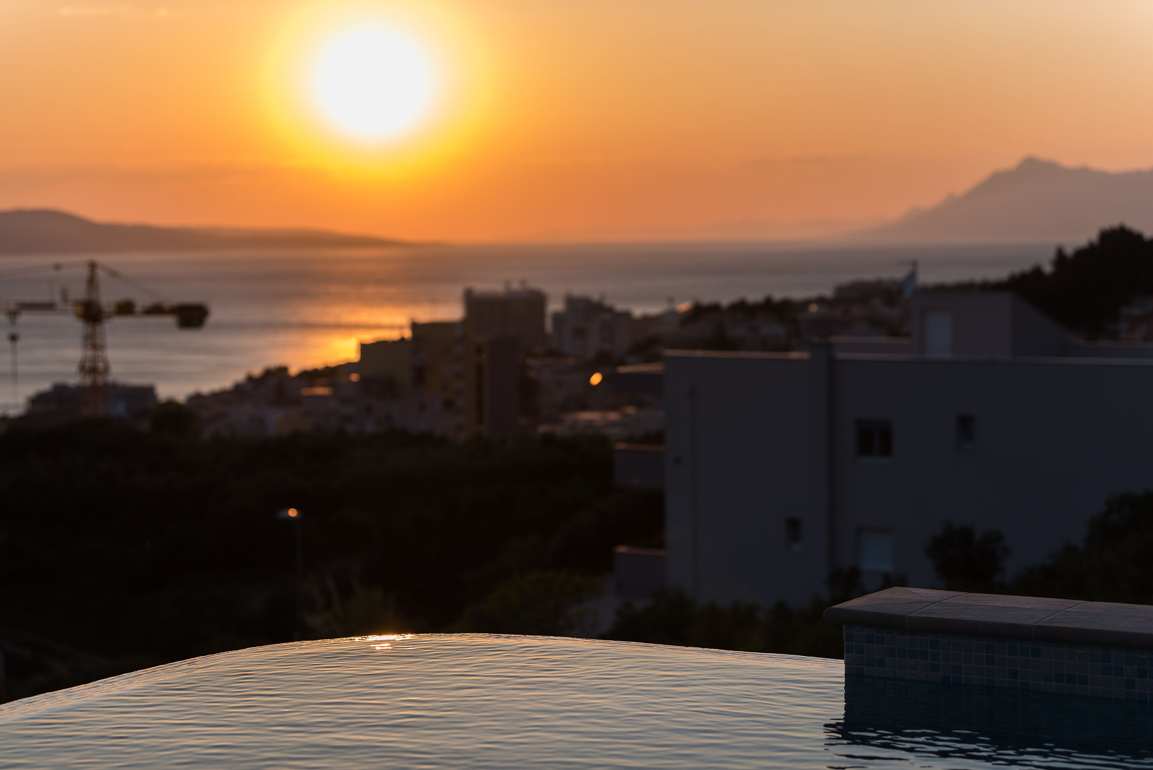 A sunset over a coastal city with buildings and a body of water.