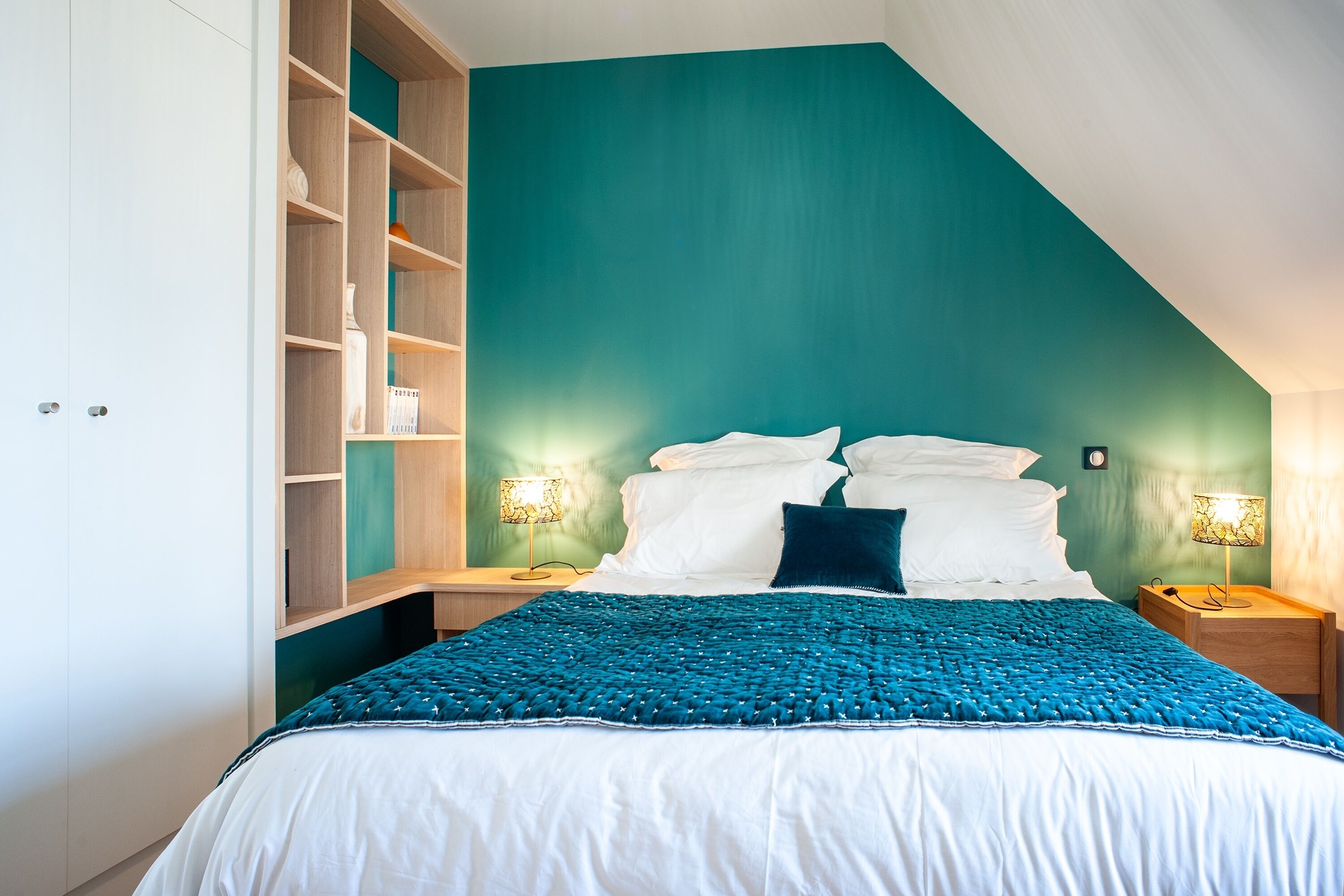 Ein Schlafzimmer mit einem Bett, zwei Nachttischen, einer Wandlampe und einer integrierten Regaleinheit.