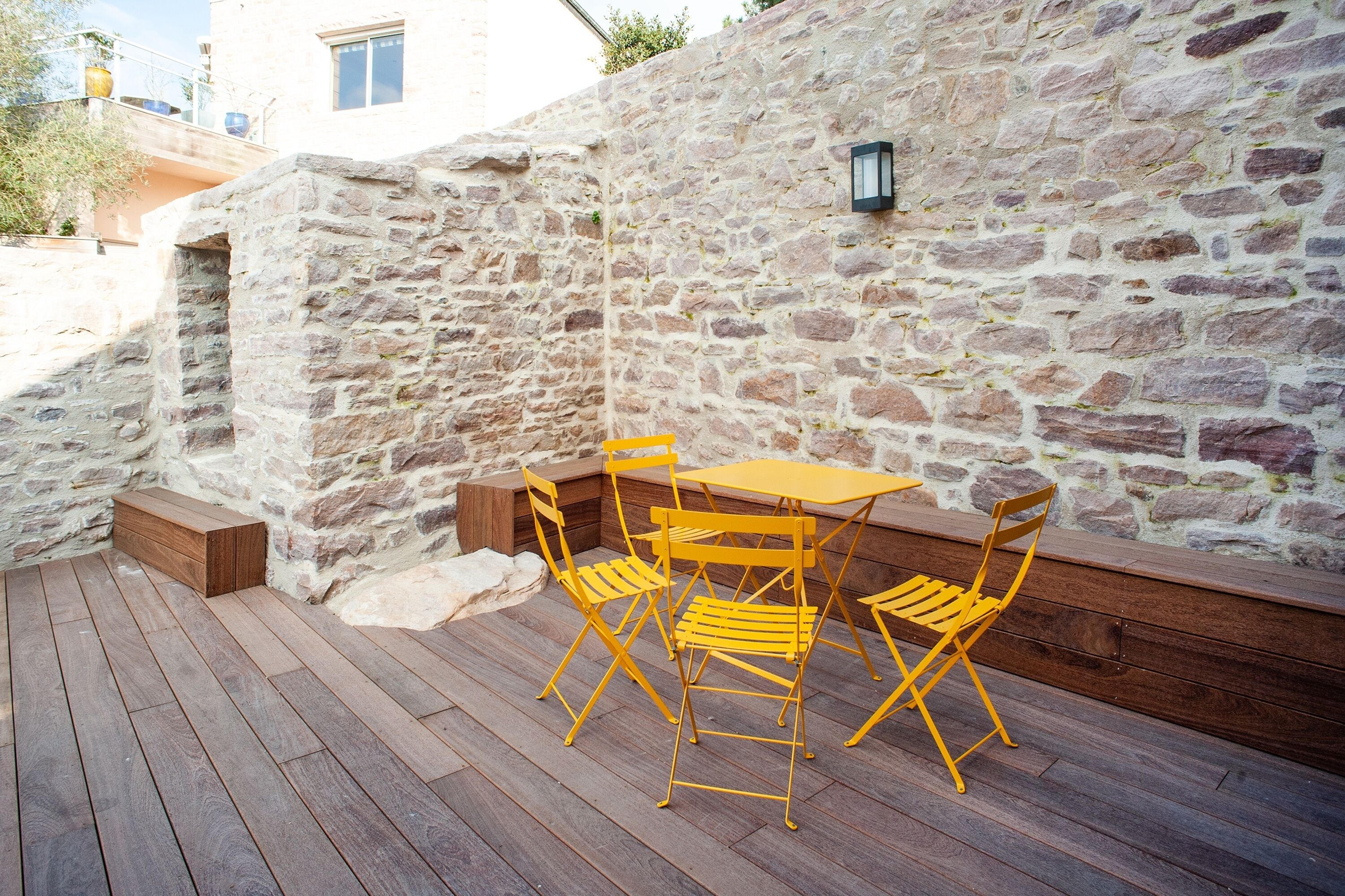 Un mur de pierre avec une terrasse en bois et des chaises jaunes.