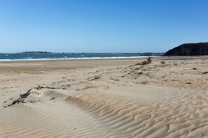 A sandy beach with gentle waves and a distant view of a town.