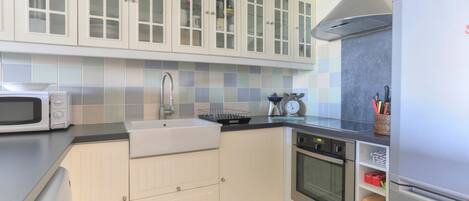 Una cocina moderna con armarios blancos, una campana extractora de acero inoxidable, un microondas, un fregadero y un refrigerador.