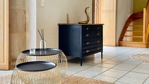 A room with a black dresser, a round table with a wireframe base, and a staircase in the background. - Tour des Alleux - Maison de maître pour 6 (Taden)