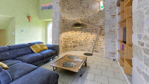 A cozy living area with a stone wall, a blue sofa, a wooden coffee table, and a floor lamp. - Tour des Alleux - Maison de maître pour 6 (Taden)