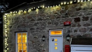 A stone building with a white door and window, illuminated by string lights. - Ranch House Cottage · Ranch House Cottage, Inverurie, Aberdeenshire (Aberdeenshire)