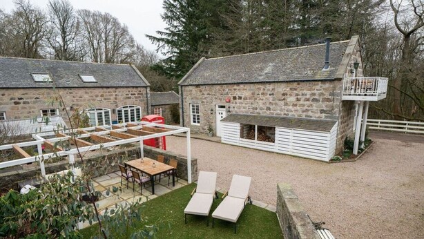 A stone building with a balcony, a covered outdoor seating area, and a fenced yard. - Ranch House Cottage · Ranch House Cottage, Inverurie, Aberdeenshire (Aberdeenshire)