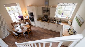 A kitchen with white cabinets, a dining table set for four, and a window with curtains. - Ranch House Cottage · Ranch House Cottage, Inverurie, Aberdeenshire (Aberdeenshire)