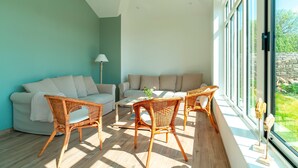 Ein helles Wohnzimmer mit einer Couch, zwei Korbstühlen, einem Couchtisch und einer Lampe.