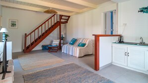 Ein Wohnzimmer mit einer Holztreppe, einem Sofa, einer Küchenzeile und einem Esstisch.
